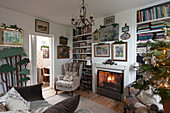 Lit fire and Christmas tree with armchair and book shelves in London home  England  UK