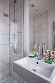 Mixer tap on washbasin with soap and shower cubicle in London home  England  UK