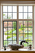 Duck ornament on leaded glass windowsill with view of Suffolk garden  England  UK