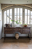 Antique wooden sideboard at arched window in Oxfordshire barn conversion  England  UK