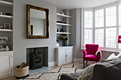 PInk armchair and gilt framed mirror with woodburner in terraced house in Whitstable   Kent  England  UK