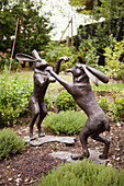 Statues of two hares playfighting on rear legs in herb garden of Amberley home, West Sussex, England, UK