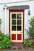 Red and yellow glass-paned front door of whitewashed Devon cottage England UK