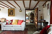 Gilt framed artwork above white sofa with bright cushions in beamed Devon cottage England UK
