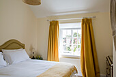 White duvet and pillows on double bed with yellow curtains in bedroom of Petworth farmhouse West Sussex Kent