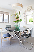 Glass-topped dining table with porcelain floor tiles in renovated 1950s coastal beach house West Sussex UK