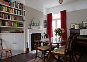 Polished wooden table and bookshelves in dining room with red velvet curtains   contemporary London home   England   UK