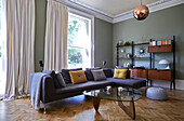 Grey corner sofa with glass topped coffee table in parquet living room of London family home,  England,  UK