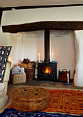 Brown leather footstool at candlelit fireplace with wood burning stove in Brabourne farmhouse,  Kent,  UK