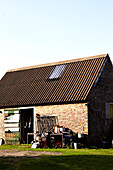 Gardening equipment at open door of brick Brabourne barn exterior,  Kent,  UK