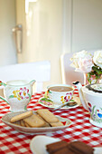 Nachmittagstee mit Keksen auf rot-weißem Tischtuch in einem Haus in Faversham, Kent, Großbritannien