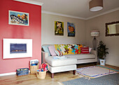 Red feature wall with print collection and colourful cushions in living room of Bolton home,  Greater Manchester,  England,  UK