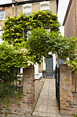View through overgrown gate with paved path to front door of London home  England  UK