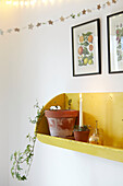 Lit candle and ivy on yellow shelf with botanic prints in London home  UK