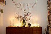 Christmas baubles on twig arrangement with lit candles on sideboard in London home  UK