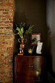Vintage ornaments on polished cabinet with exposed brick wall in East London townhouse  England  UK