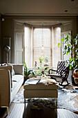 Sofa and ottoman with buttoned brown leather rocking chair in bay window of East London townhouse  England  UK