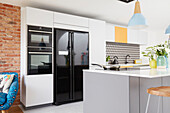 Moderne mehrfarbige Einbauküche mit schwarzen Geräten und geometrischer Spritzschutzwand London UK