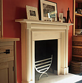 Close up of traditional white fireplace with cast iron grate in bright red living room