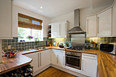 Edelstahl-Dunstabzugshaube über dem Backofen in einer weißen Einbauküche in einem Haus in New Malden, Surrey, England, UK