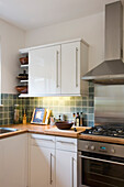 Dunstabzugshaube aus Edelstahl über dem Kochfeld in einer weißen Einbauküche in einem Haus in New Malden, Surrey, England, UK