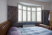 Doppelbett am Fenster mit Fensterläden im Schlafzimmer in einem Haus in New Malden, Surrey, England, UK