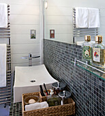 Waschbecken und Korb mit Toilettenartikeln unter dem Spiegel in der grau gefliesten Nasszelle einer Wassermühle