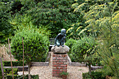 Gravel herb garden with raised beds and sculpture of a boy in Essex garden UK