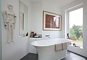 Freistehende Badewanne mit moderner Kunst und Spiegel an einem großen Fenster in einem Haus in Essex, Großbritannien