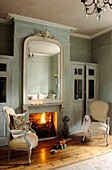 Open fire in soft blue grey living room with French fauteuils