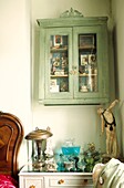 Dressing table with array of coloured glass flacons and wall mounted antique green cupboard