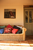 Cane sofa with loose cushions on terracotta floor tiles
