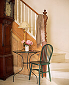 Grandfather clock stands next to table and chair at the base of the stripped pine stairs