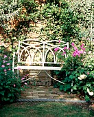 White garden bench in domestic garden with flowers