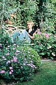 Frau lehnt sich auf einer Gartenbank neben Blumenbeeten zurück
