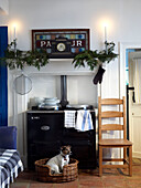 Hund sitzt im Körbchen neben dem Ofen mit festlicher Dekoration auf dem Kaminsims darüber
