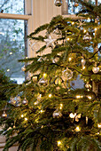 Weihnachtsbaumschmuck mit Glaskugeln, Silberkugeln und Lichterketten am Fenster