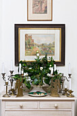 Side table with assorted metallic candlesticks and vase filled with ivy and white flowers