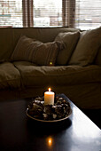 Lit Christmas candle on table with sofa upholstered with natural fabric
