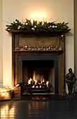 Lit fire and candles with garland on wooden fireplace