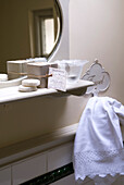 Soaps on bathroom shelf with white towel and oval-shaped mirror