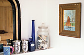 Silver goblets and blue glass with seashells on shelf in bathroom with nautical artwork