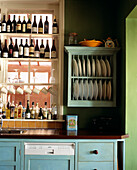 Bottles of wine and liqueurs above kitchen sink next to plate rack