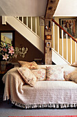 Holzbalken und Treppe im Cottage-Wohnzimmer mit cremefarbenem Sofa und blumengemusterten Kissen