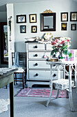 Cameos and artwork with mirror above painted chest of drawers in cottage bedroom