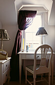 Schreibtisch und Lampe in einer Fensternische mit dunkelrotem, ungefüttertem Seidenvorhang