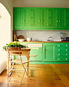 Green painted kitchen cabinets with cut foliage on table at window 