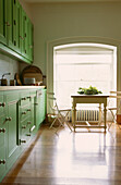 Grün gestrichene Küchenschränke mit Tisch und Klappstühlen vor einem palladianischen Fenster aus dem 18