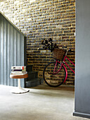 Pink bicycle with basket leaning on exposed brick wall in hallway