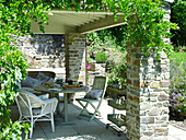 Outdoor room covered in wisteria with shaded table set for breakfast 